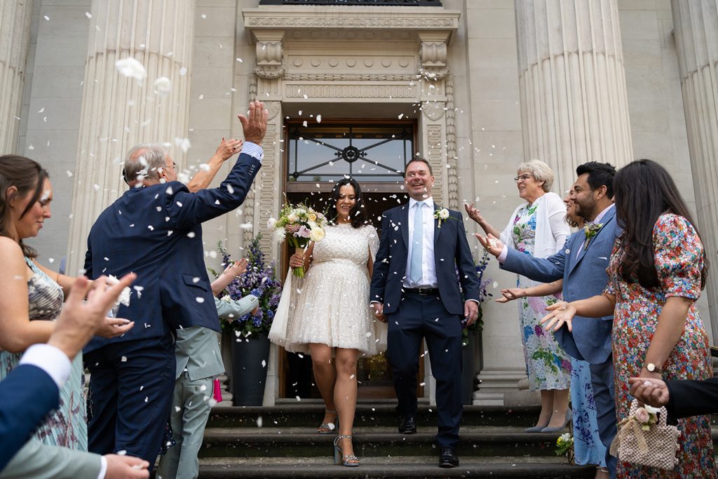 bride and groom exit the old Marylebone Town hall while guests throw confetti